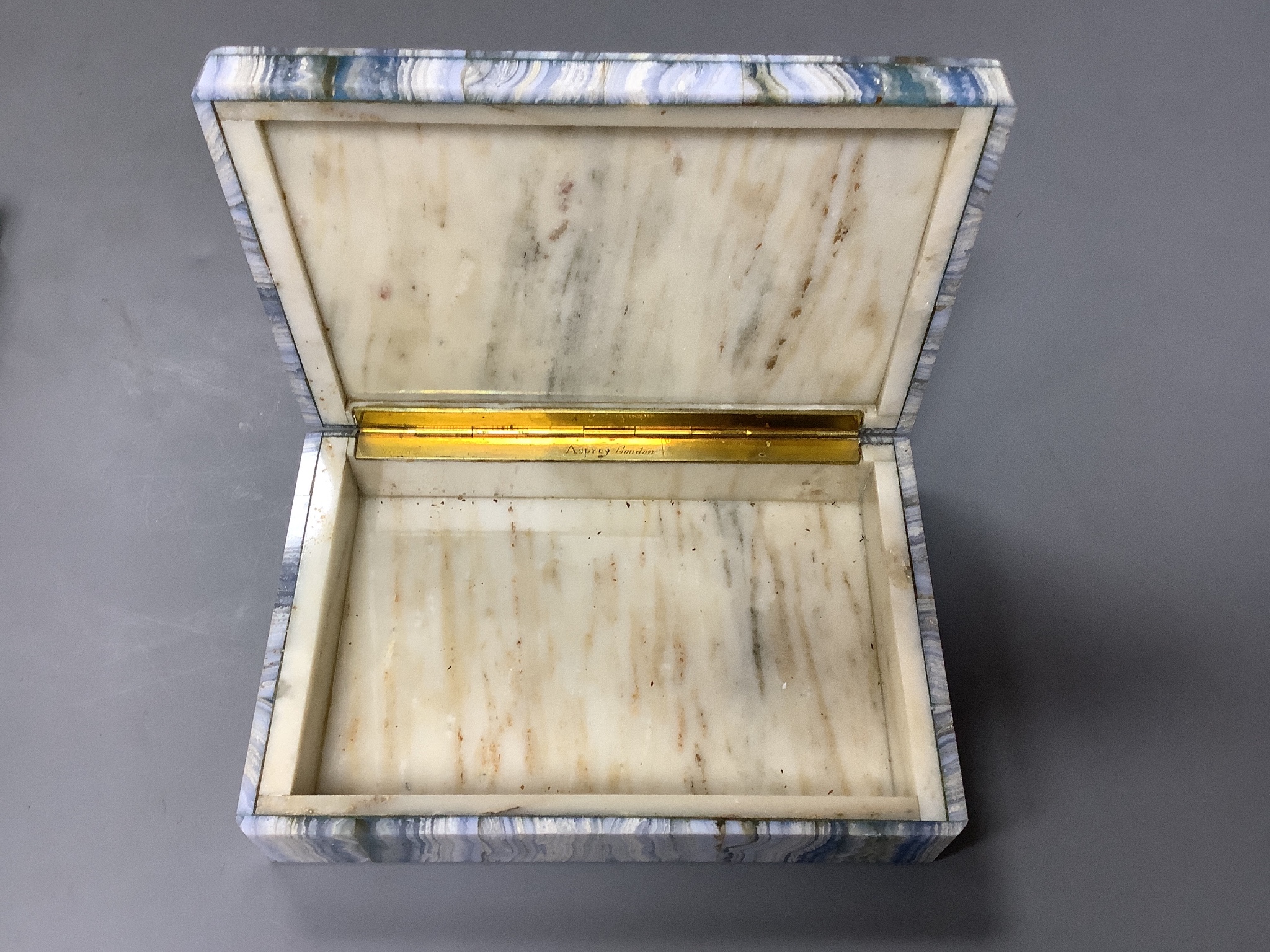 Two specimen marble cigarette boxes, 15cm and a similar blue agate cigarette box, 15.5cm, all three retailed by Asprey London and signed to the hinge mount